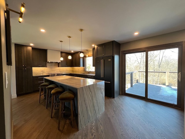 kitchen featuring dark brown cabinets, a kitchen island, decorative backsplash, and wood finished floors