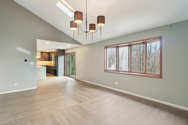 unfurnished room with a notable chandelier, lofted ceiling with skylight, plenty of natural light, and wood finished floors