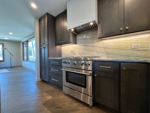 kitchen featuring stainless steel stove, baseboards, wall chimney range hood, decorative backsplash, and dark wood finished floors