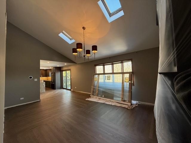 unfurnished living room with high vaulted ceiling, baseboards, a skylight, and a chandelier