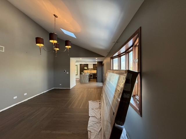 interior space featuring a chandelier, vaulted ceiling with skylight, baseboards, and parquet flooring