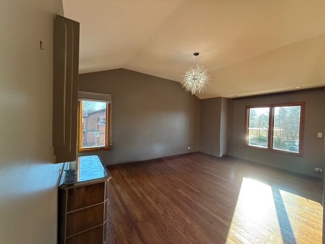 empty room with a notable chandelier, vaulted ceiling, and wood finished floors