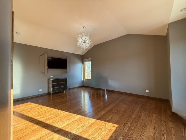 unfurnished living room with a chandelier, vaulted ceiling, and wood finished floors