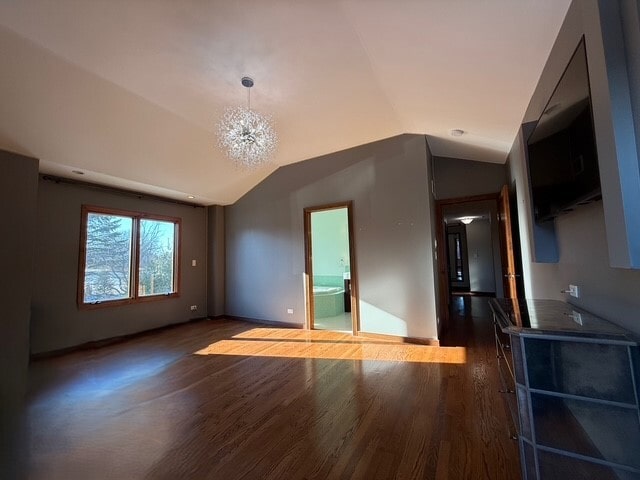 unfurnished room with baseboards, vaulted ceiling, an inviting chandelier, and wood finished floors