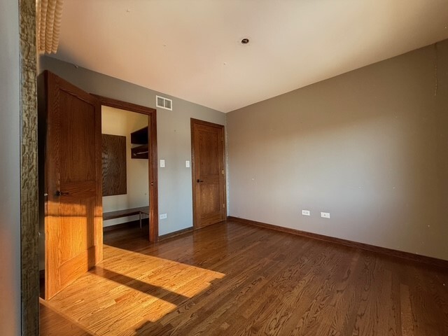 unfurnished bedroom with wood finished floors, visible vents, and baseboards