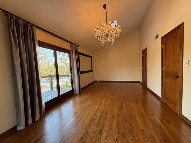 empty room with a chandelier, high vaulted ceiling, visible vents, baseboards, and dark wood-style floors