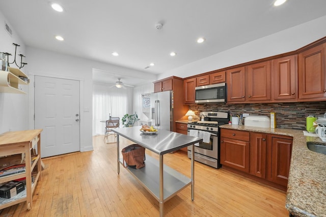 kitchen featuring backsplash, light stone counters, stainless steel appliances, ceiling fan, and light hardwood / wood-style floors