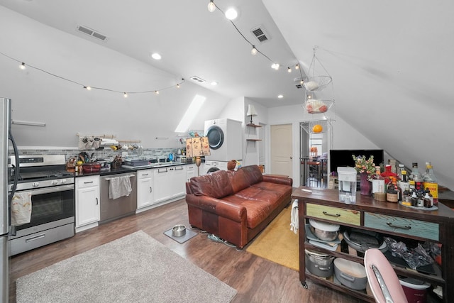 kitchen with lofted ceiling, white cabinets, decorative backsplash, appliances with stainless steel finishes, and stacked washer / drying machine