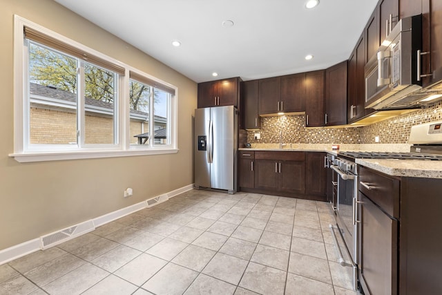 kitchen with dark brown cabinetry, light stone counters, light tile patterned floors, and stainless steel appliances