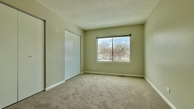 unfurnished bedroom featuring a textured ceiling, multiple closets, and light colored carpet