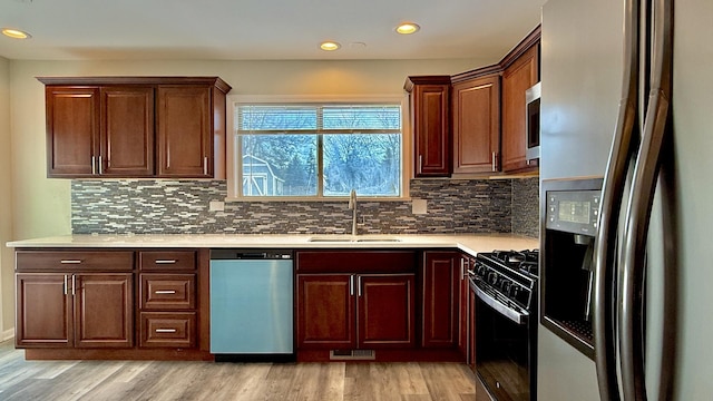 kitchen featuring appliances with stainless steel finishes, light hardwood / wood-style floors, tasteful backsplash, and sink