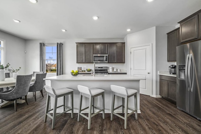 kitchen featuring stainless steel appliances, dark hardwood / wood-style floors, dark brown cabinetry, and a kitchen island with sink