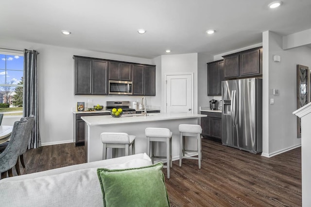 kitchen with stainless steel appliances, sink, a center island with sink, dark brown cabinets, and a breakfast bar area