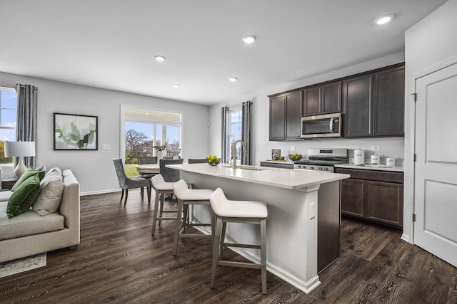 kitchen with a breakfast bar, sink, dark brown cabinetry, an island with sink, and stainless steel appliances