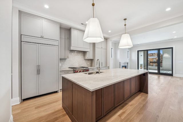 kitchen featuring pendant lighting, sink, paneled built in refrigerator, a kitchen island with sink, and light stone countertops