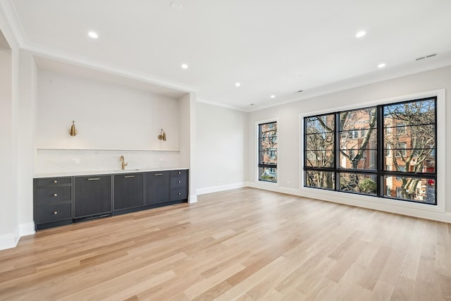 unfurnished living room featuring ornamental molding, indoor wet bar, and light hardwood / wood-style floors