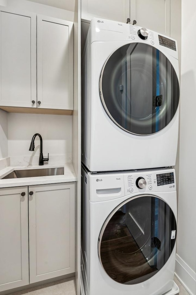 washroom with cabinets, stacked washing maching and dryer, and sink