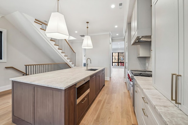 kitchen featuring sink, hanging light fixtures, appliances with stainless steel finishes, a kitchen island with sink, and white cabinets