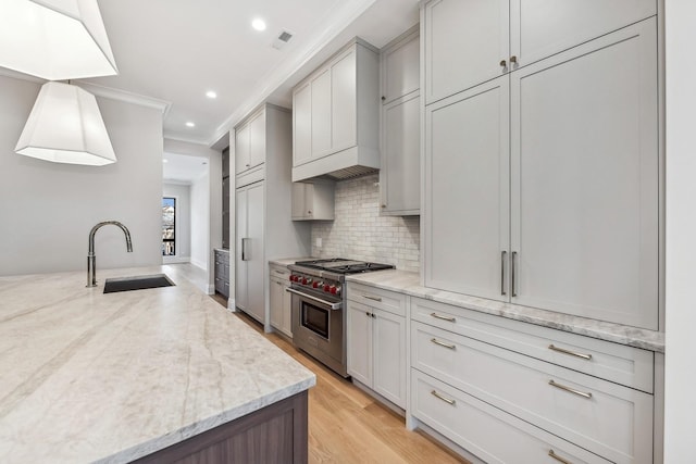 kitchen with pendant lighting, sink, high end range, light stone countertops, and custom exhaust hood