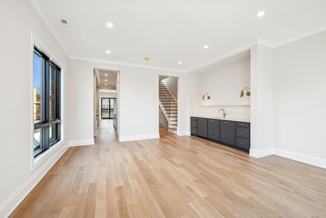 unfurnished living room with light hardwood / wood-style flooring, ornamental molding, and indoor wet bar