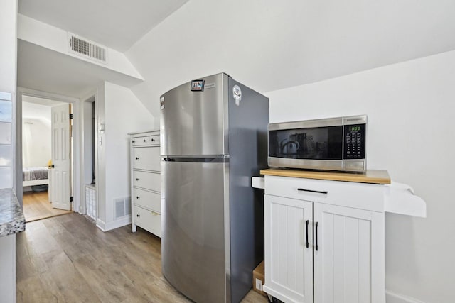 kitchen featuring white cabinets, stainless steel appliances, vaulted ceiling, and light wood-type flooring