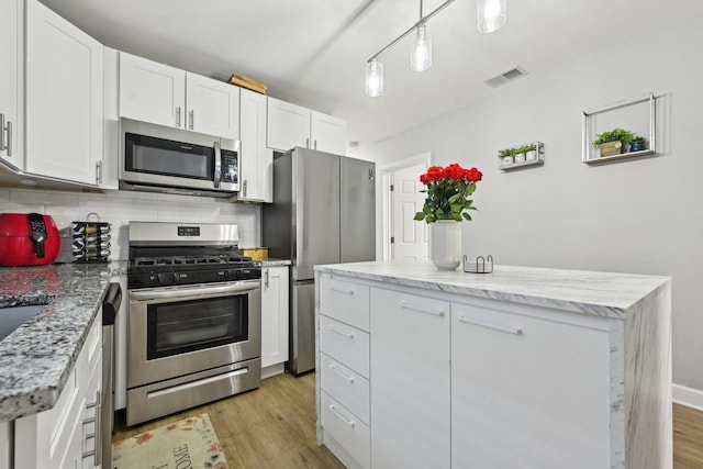 kitchen featuring hanging light fixtures, light wood-type flooring, white cabinetry, decorative backsplash, and stainless steel appliances