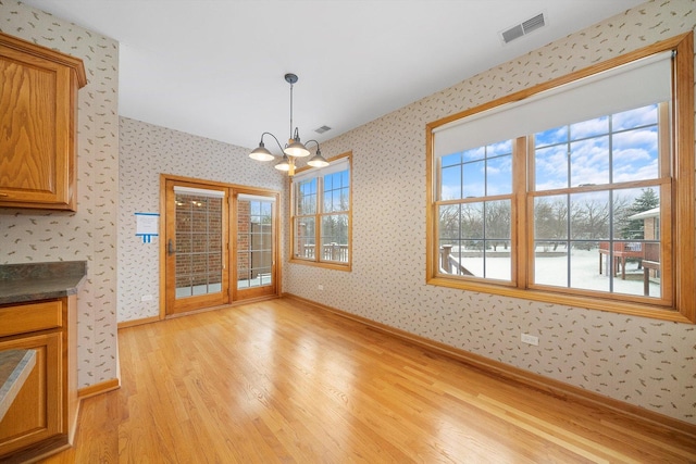 unfurnished living room with light wood-type flooring and an inviting chandelier