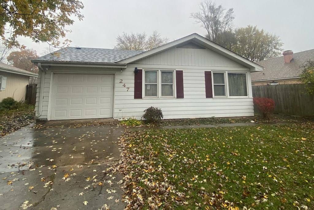 ranch-style home with concrete driveway, roof with shingles, an attached garage, fence, and a front yard