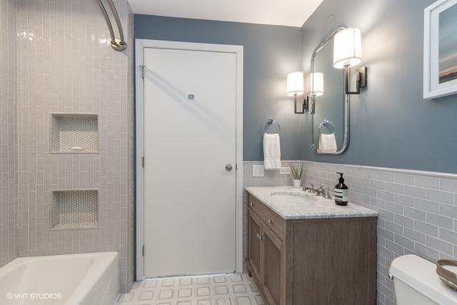 full bathroom with tile walls, tiled shower / bath combo, vanity, and toilet