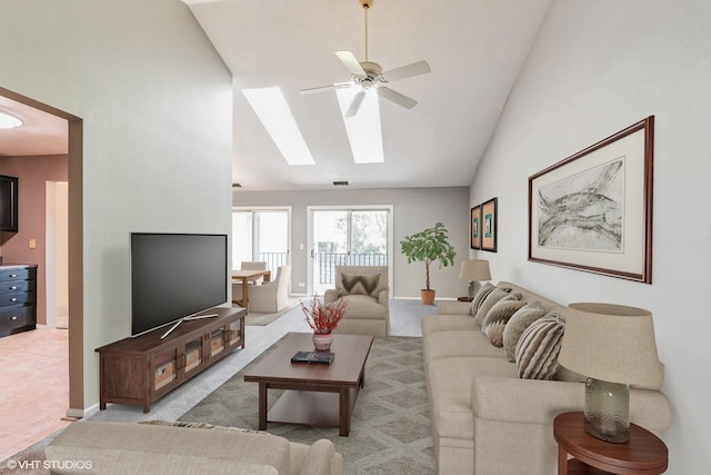 living room with vaulted ceiling with skylight, ceiling fan, and light colored carpet