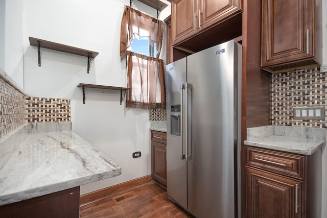 kitchen featuring light stone counters, dark hardwood / wood-style flooring, stainless steel fridge with ice dispenser, and backsplash