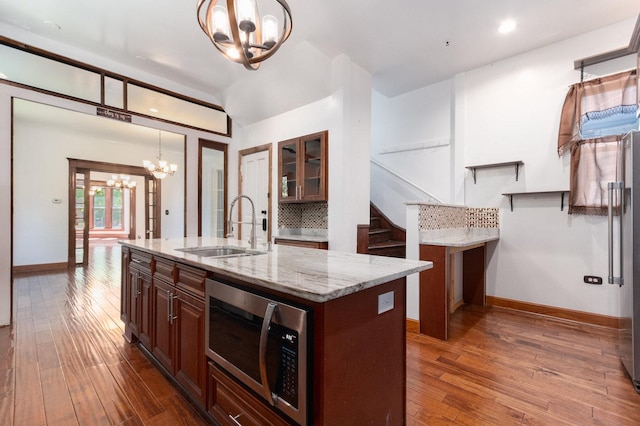 kitchen with an inviting chandelier, a center island with sink, sink, hanging light fixtures, and light stone countertops