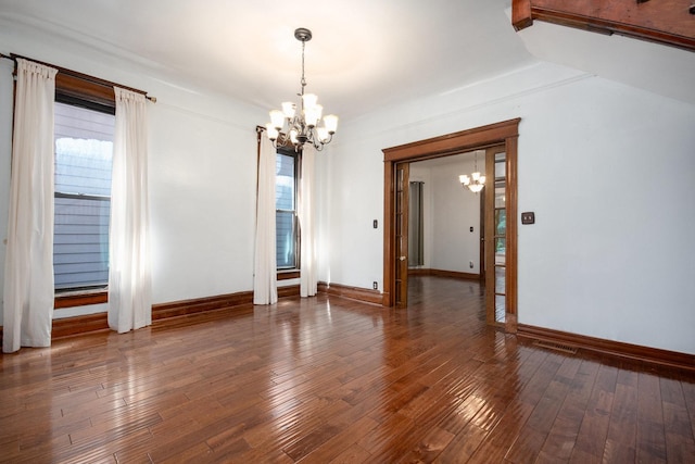 spare room with an inviting chandelier, a wealth of natural light, and dark wood-type flooring