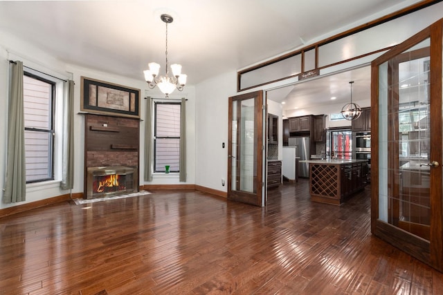 unfurnished living room featuring french doors, a healthy amount of sunlight, dark wood-type flooring, a notable chandelier, and a fireplace