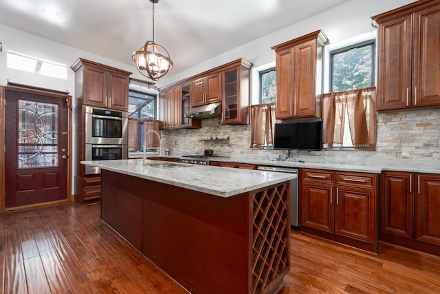 kitchen featuring decorative backsplash, appliances with stainless steel finishes, a kitchen island with sink, decorative light fixtures, and a chandelier