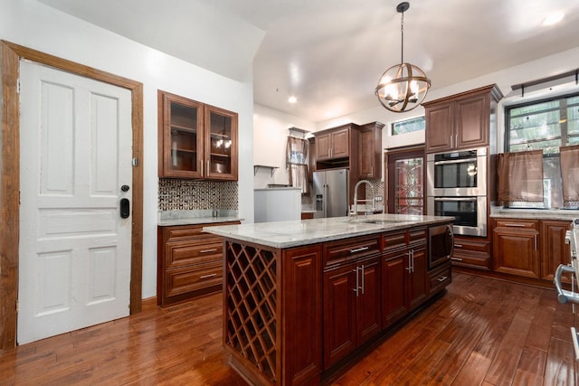 kitchen featuring appliances with stainless steel finishes, tasteful backsplash, a center island with sink, an inviting chandelier, and hanging light fixtures