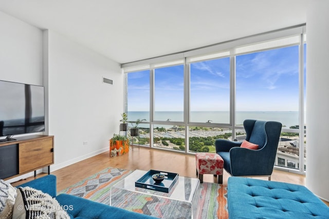 living room with expansive windows, a wealth of natural light, a water view, and hardwood / wood-style flooring