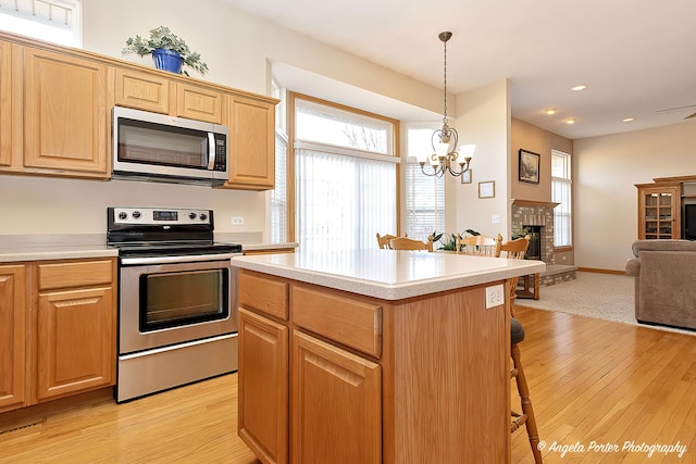 kitchen with an inviting chandelier, decorative light fixtures, a kitchen bar, a fireplace, and appliances with stainless steel finishes