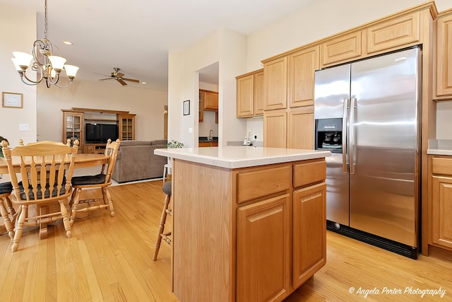 kitchen with a center island, stainless steel fridge, light hardwood / wood-style floors, decorative light fixtures, and ceiling fan with notable chandelier