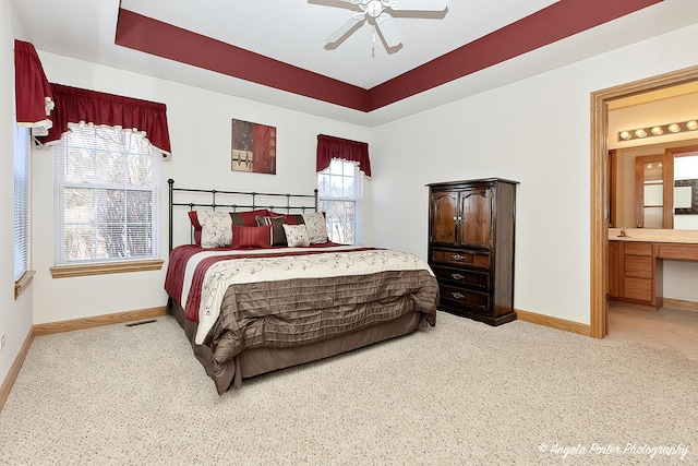 carpeted bedroom with a tray ceiling, ensuite bathroom, and ceiling fan