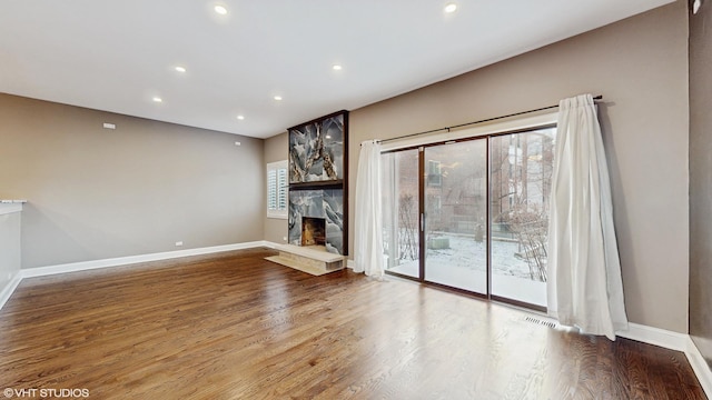 unfurnished living room with hardwood / wood-style flooring and a stone fireplace