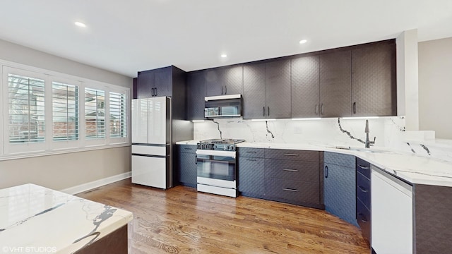 kitchen featuring light stone countertops, sink, light hardwood / wood-style flooring, backsplash, and white appliances