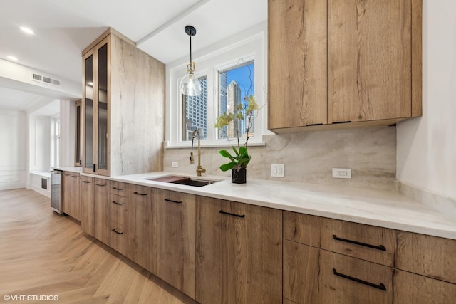 kitchen with tasteful backsplash, light parquet floors, beverage cooler, sink, and pendant lighting