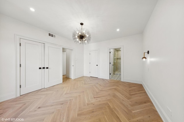 unfurnished bedroom featuring ensuite bathroom, a closet, light parquet floors, and a chandelier