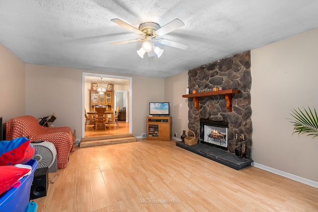 living room with hardwood / wood-style floors, ceiling fan, a stone fireplace, and a textured ceiling