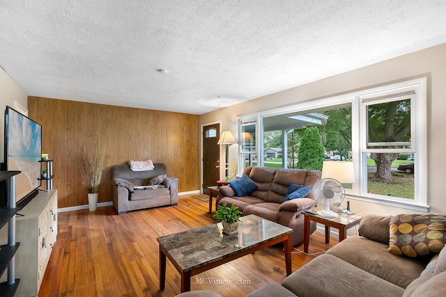 living room featuring a textured ceiling, light wood-type flooring, and wood walls