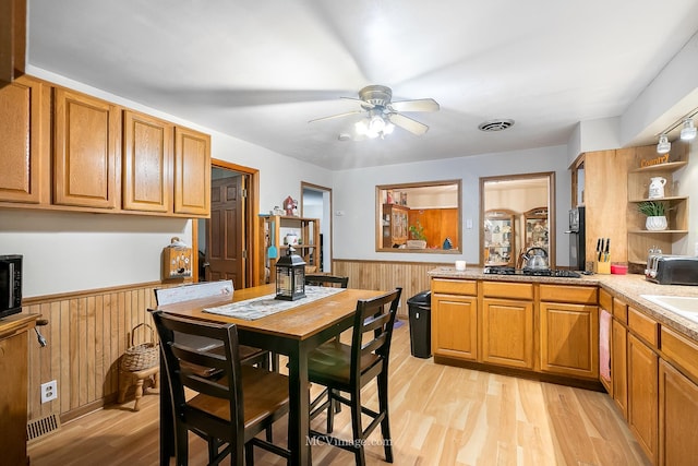 kitchen with wood walls, black appliances, sink, ceiling fan, and light hardwood / wood-style floors