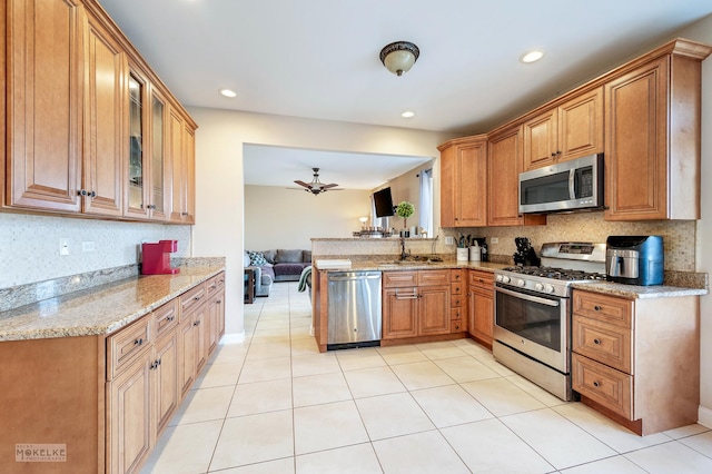 kitchen with backsplash, glass insert cabinets, light stone counters, appliances with stainless steel finishes, and a peninsula