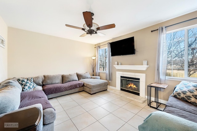 living area with a glass covered fireplace, light tile patterned floors, a ceiling fan, and baseboards