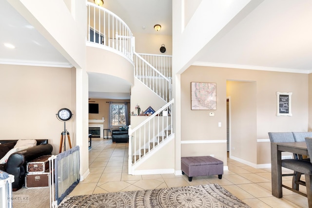 tiled entryway with ornamental molding, a high ceiling, a fireplace, baseboards, and stairs